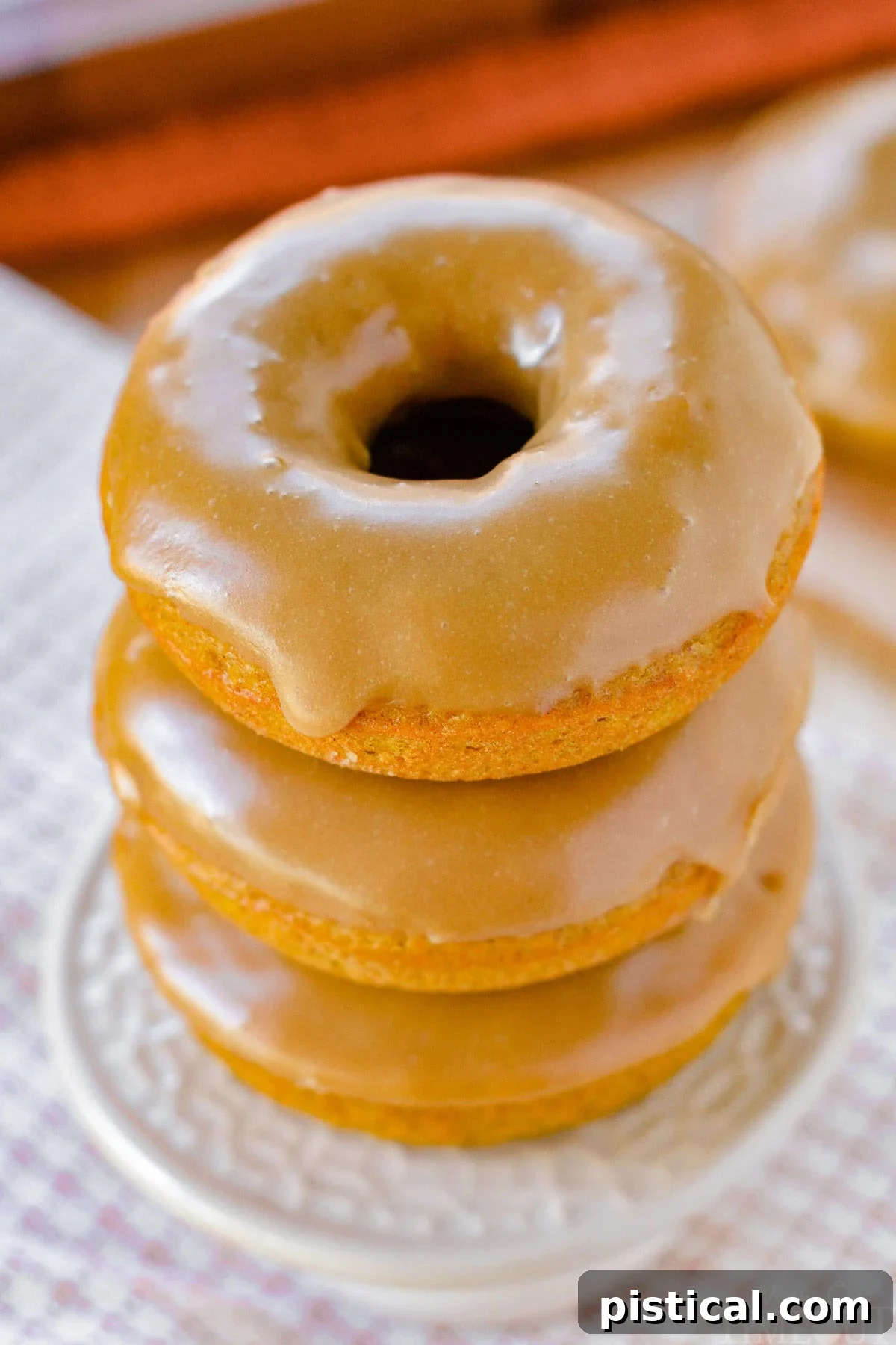 An inviting top-down angled view of three baked pumpkin donuts, perfectly stacked on a charming cupcake stand, ready to be enjoyed.