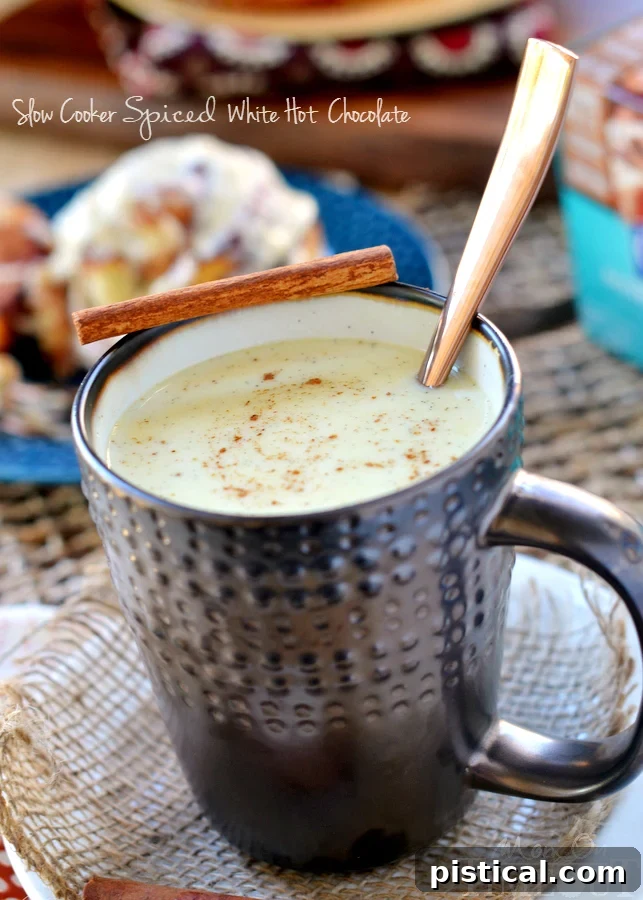 Close-up of a mug of Slow Cooker Spiced White Hot Chocolate with spices floating on top, highlighting the creamy texture and rich color.