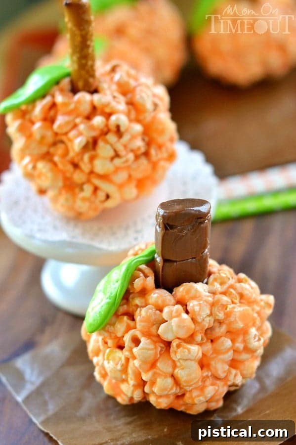 Spiced Pumpkin Popcorn Treats 3 Close-up of a festive orange Pumpkin Popcorn Ball with a green candy leaf and pretzel stem, highlighting its soft, chewy texture and homemade charm.
