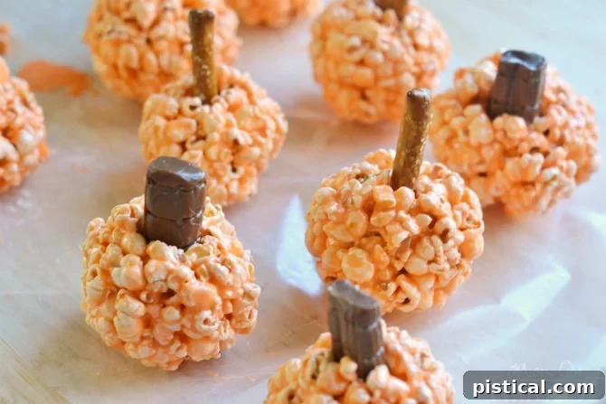 Spiced Pumpkin Popcorn Treats 4 Three perfectly formed orange Pumpkin Popcorn Balls, one with a green candy leaf, ready for festive celebrations.