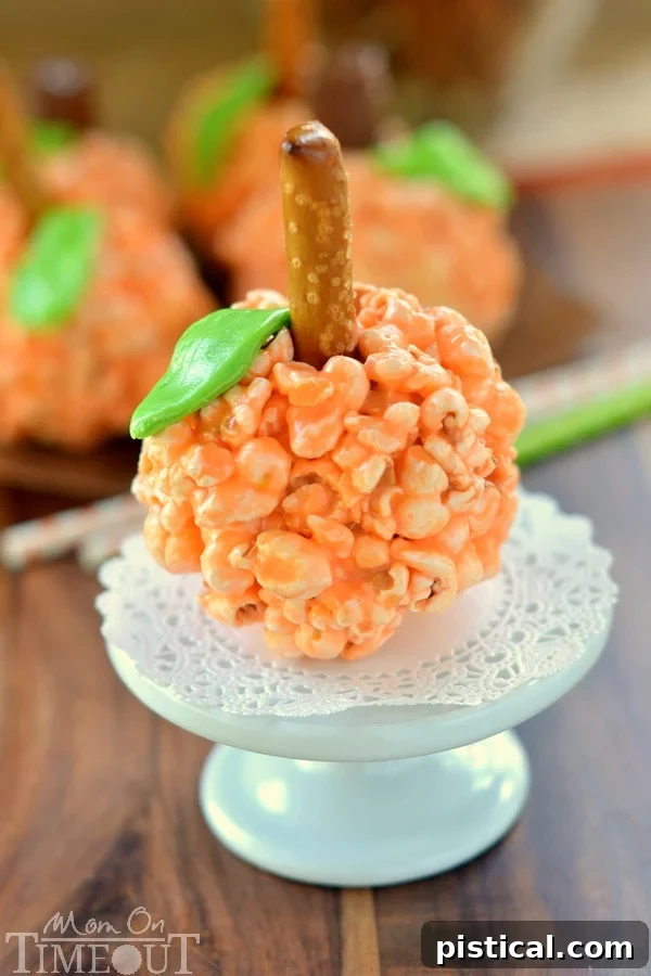 Spiced Pumpkin Popcorn Treats 5 Assortment of decorated Pumpkin Popcorn Balls with green leaves and pretzel/candy stems, arranged on a rustic wooden surface for a cozy fall vibe.