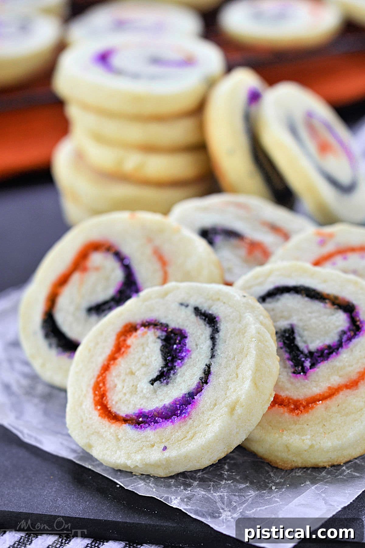 A stack of beautifully spiraled Halloween Sugar Cookies featuring orange, black, and purple sugar. Five cookies are fanned out in front, showcasing their intricate and neat spiral design.