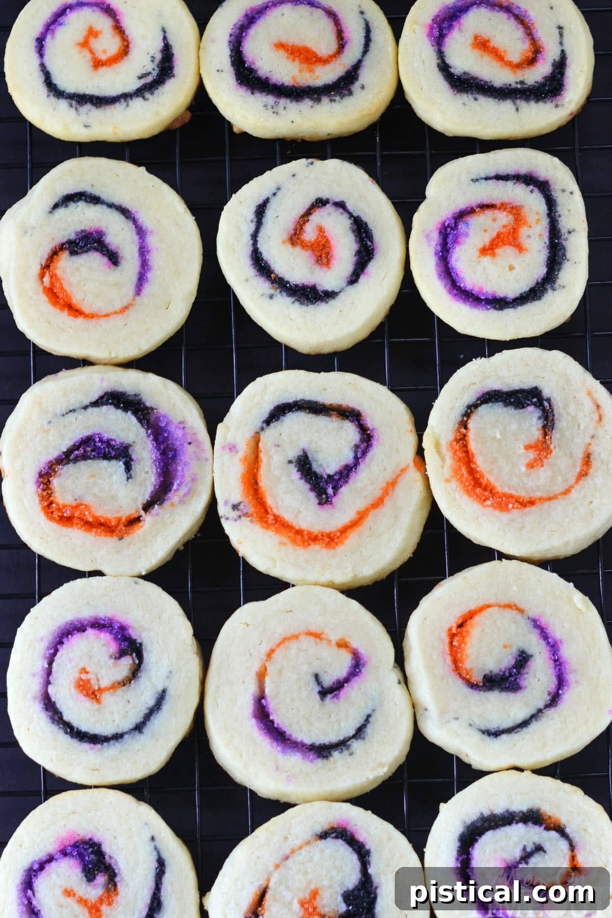 A top-down view of freshly baked spiral slice and bake Halloween cookies cooling on a black wire rack, showcasing their distinct colorful swirls.