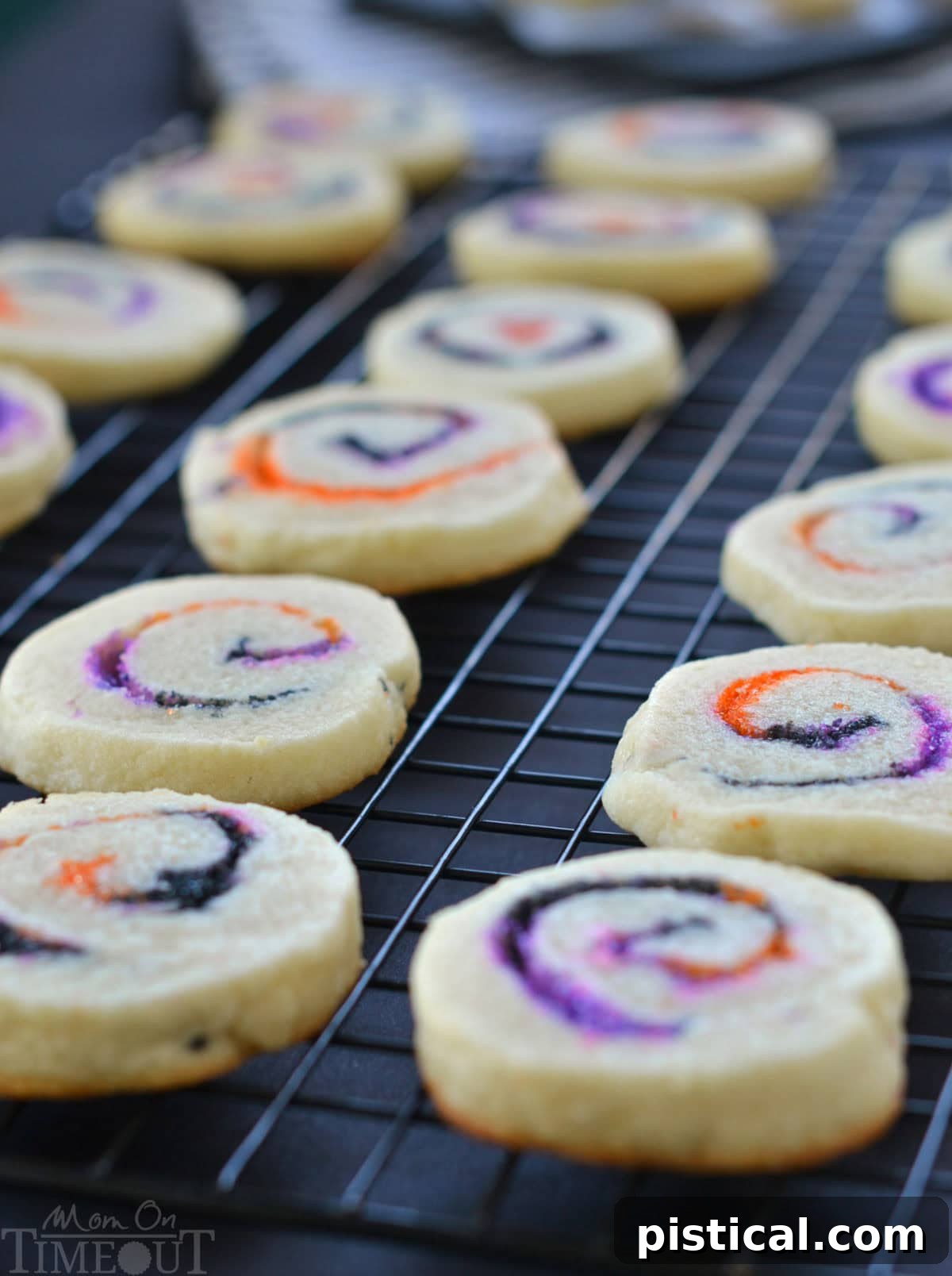 Baked Halloween cookies cooling on a black wire rack, clearly displaying the vibrant orange, black, and purple sugar swirls.