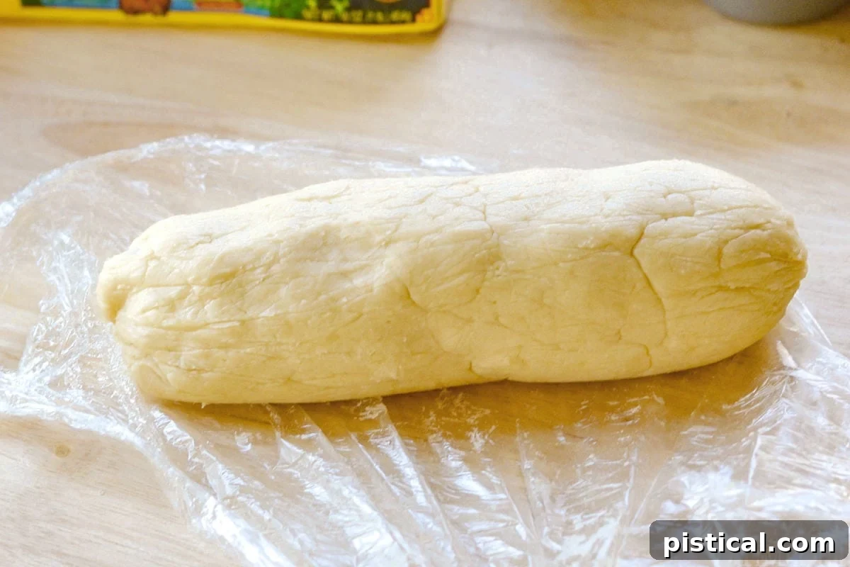 The homemade cream cheese pie crust, perfectly rolled and shaped into a log, awaiting its chilling time in the refrigerator. This visual step highlights the preparation of the tender, flaky base for the mini pecan pies.
