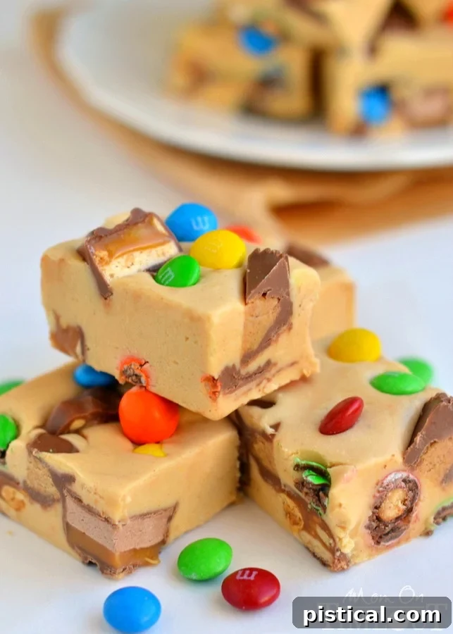 Loaded Peanut Butter Candy Bar Fudge 4 Several squares of homemade Peanut Butter Candy Bar Fudge stacked on a white plate, revealing the generous inclusion of chopped candy bars and a smooth, creamy texture. An ideal treat for sharing.