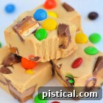 Loaded Peanut Butter Candy Bar Fudge 5 Four pieces of Peanut Butter Candy Bar Fudge stacked on a white surface with a bite taken out of the top piece.