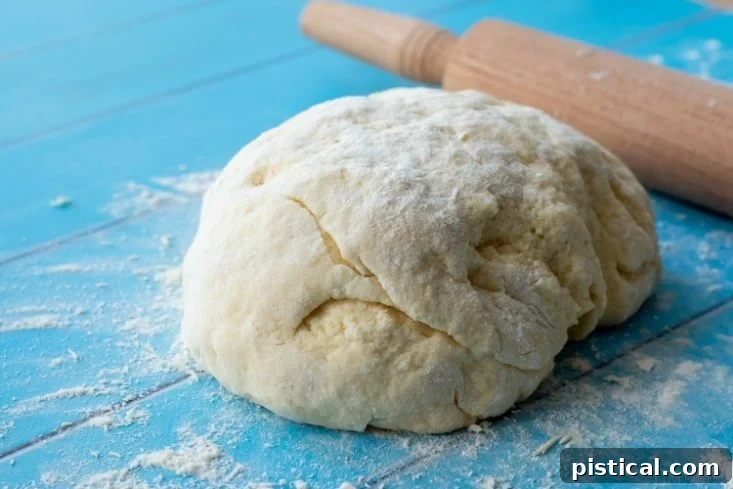 Biscuit dough being rolled out on a generously floured surface with a wooden rolling pin, meticulously prepared for cutting into perfect shapes.