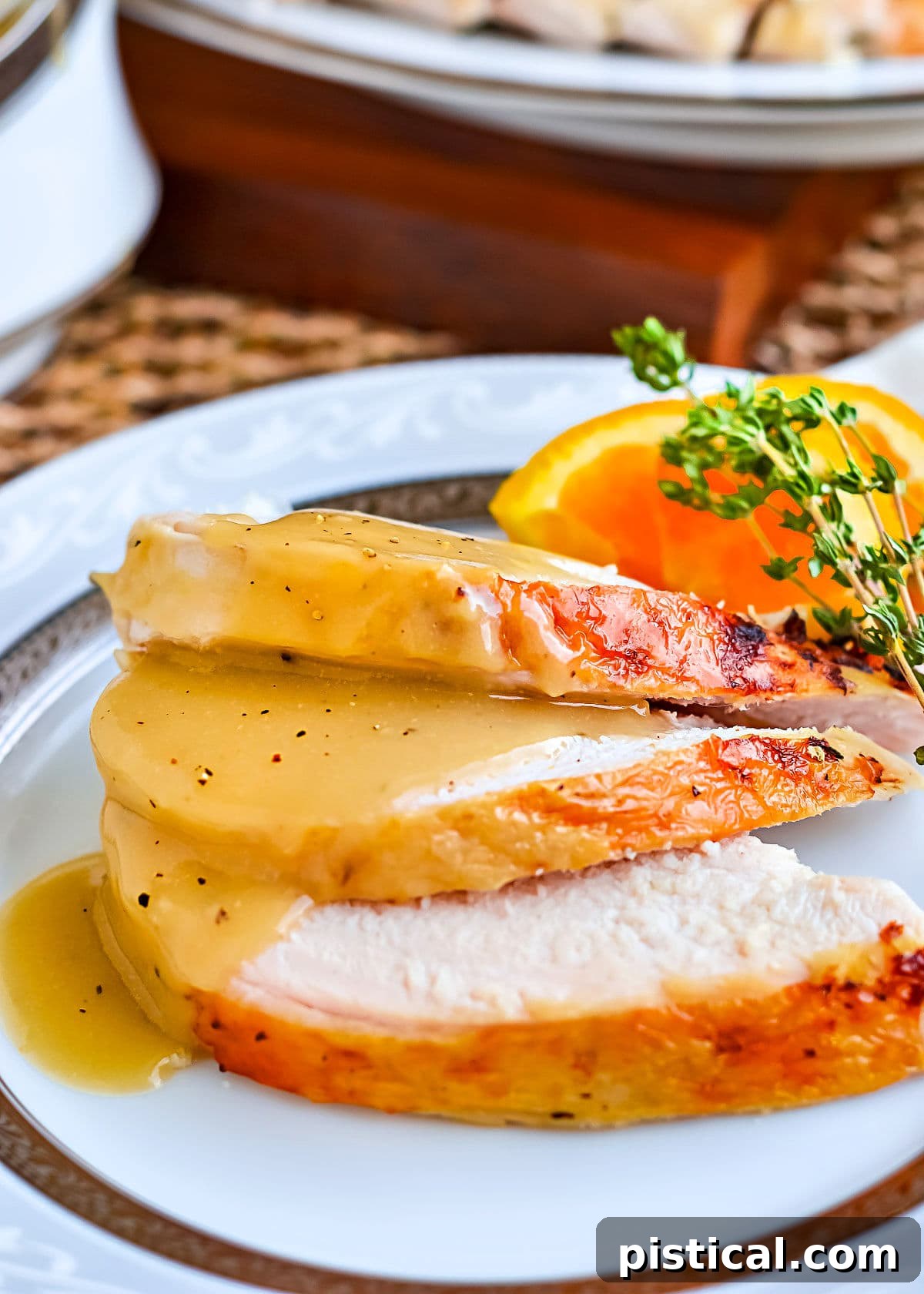 Secrets to Irresistible Turkey Gravy 3 Three succulent slices of turkey breast elegantly arranged on a white china plate with a decorative border, generously topped with a rich, silky smooth brown turkey gravy.