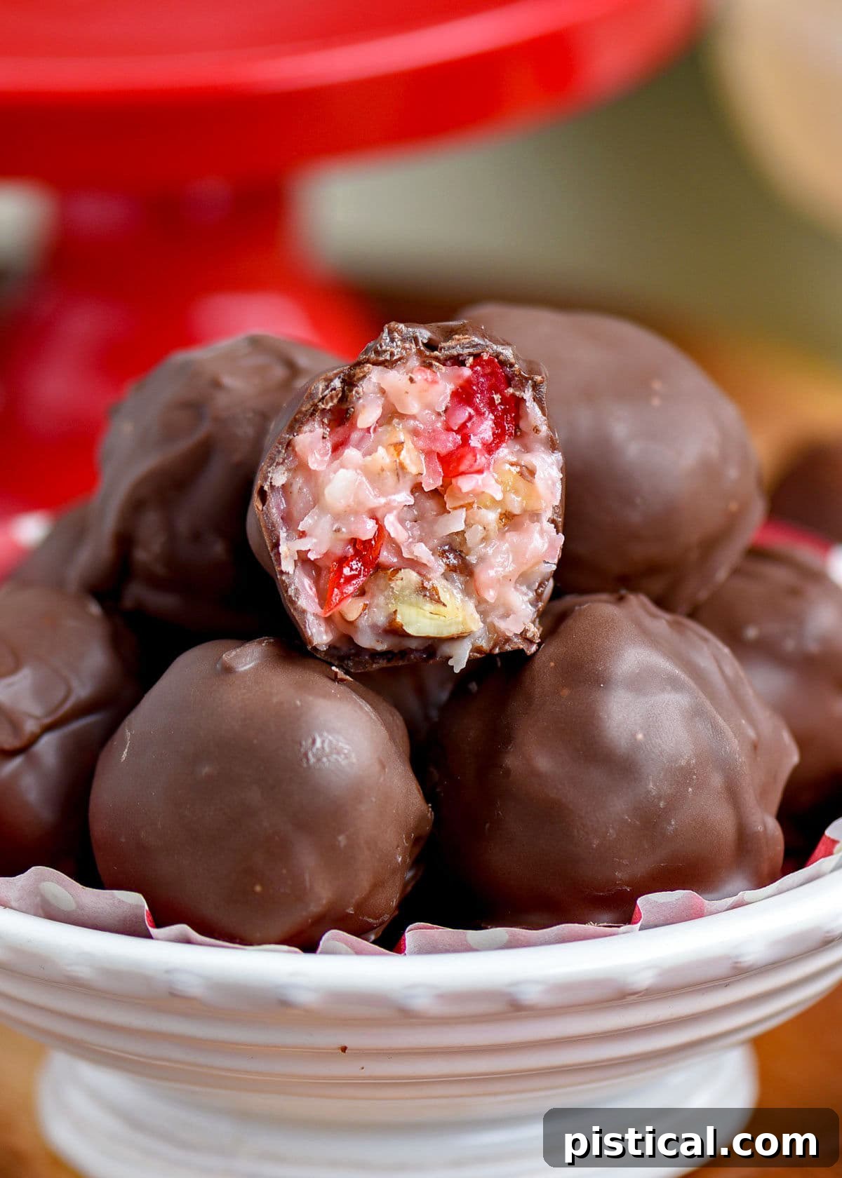 A charming white bowl filled with Martha Washington candies, with one candy halved to showcase its rich, textured interior. A festive red cake stand is visible in the background.