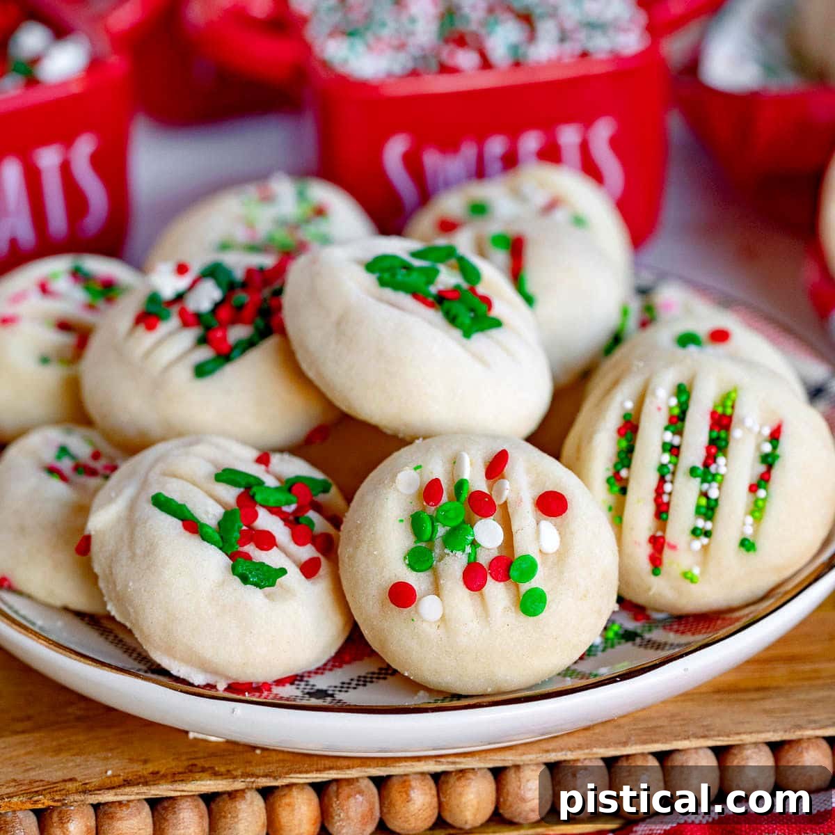 whipped shortbread cookies on a Christmas plate with red, green and white sprinkles. Plate is on cutting board sitting next to a Christmas towel.