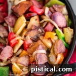 Kielbasa and potatoes in a cast iron skillet ready to be enjoyed. Skillet is resting on a red napkin. Peppers, onions, potatoes and kielbasa are all cut into bite sized pieces.