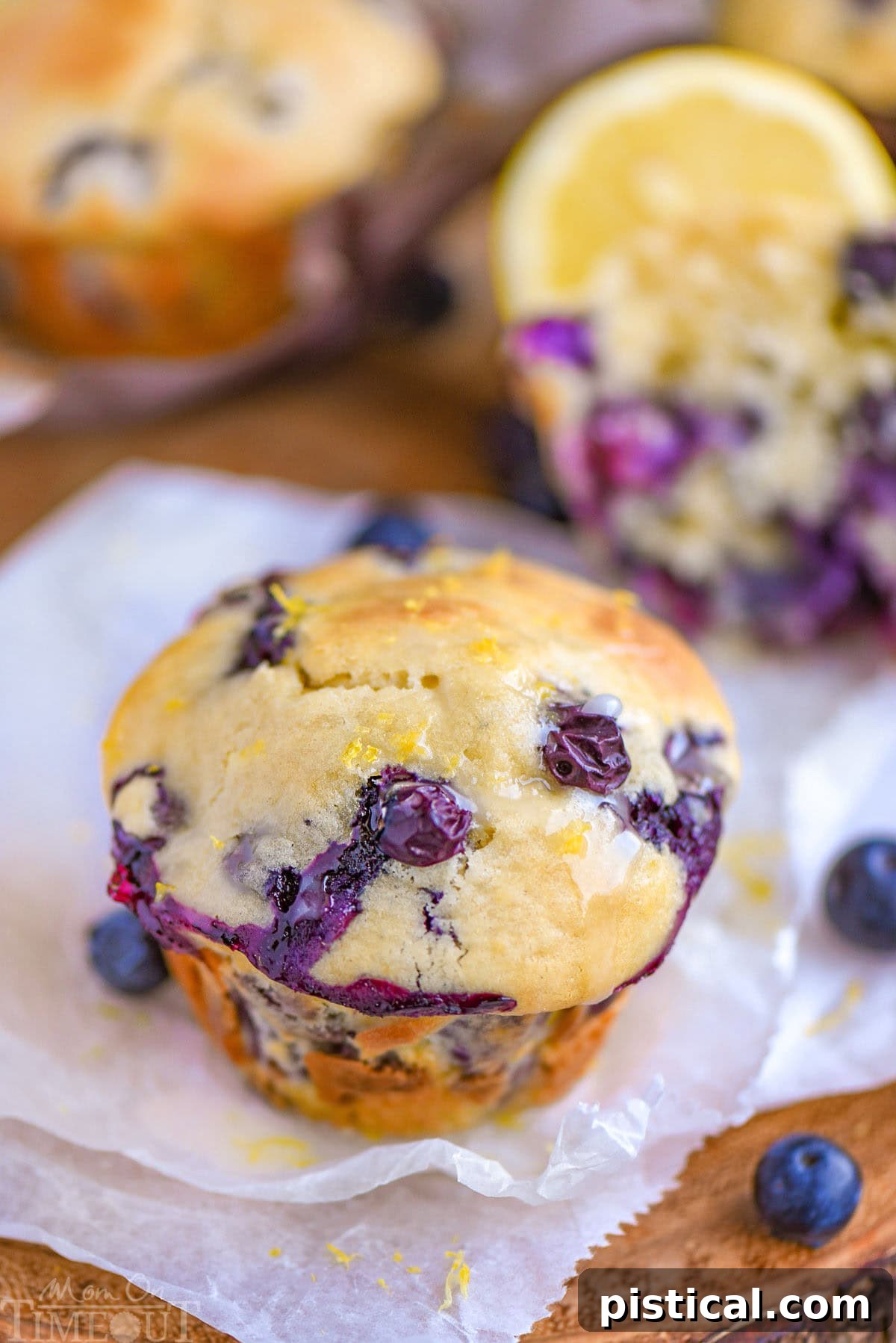 Zesty Lemon Blueberry Muffins with Cream Cheese Swirl 6 Blueberry Lemon Cream Cheese Muffins topped with a lemon glaze resting on white parchment paper.