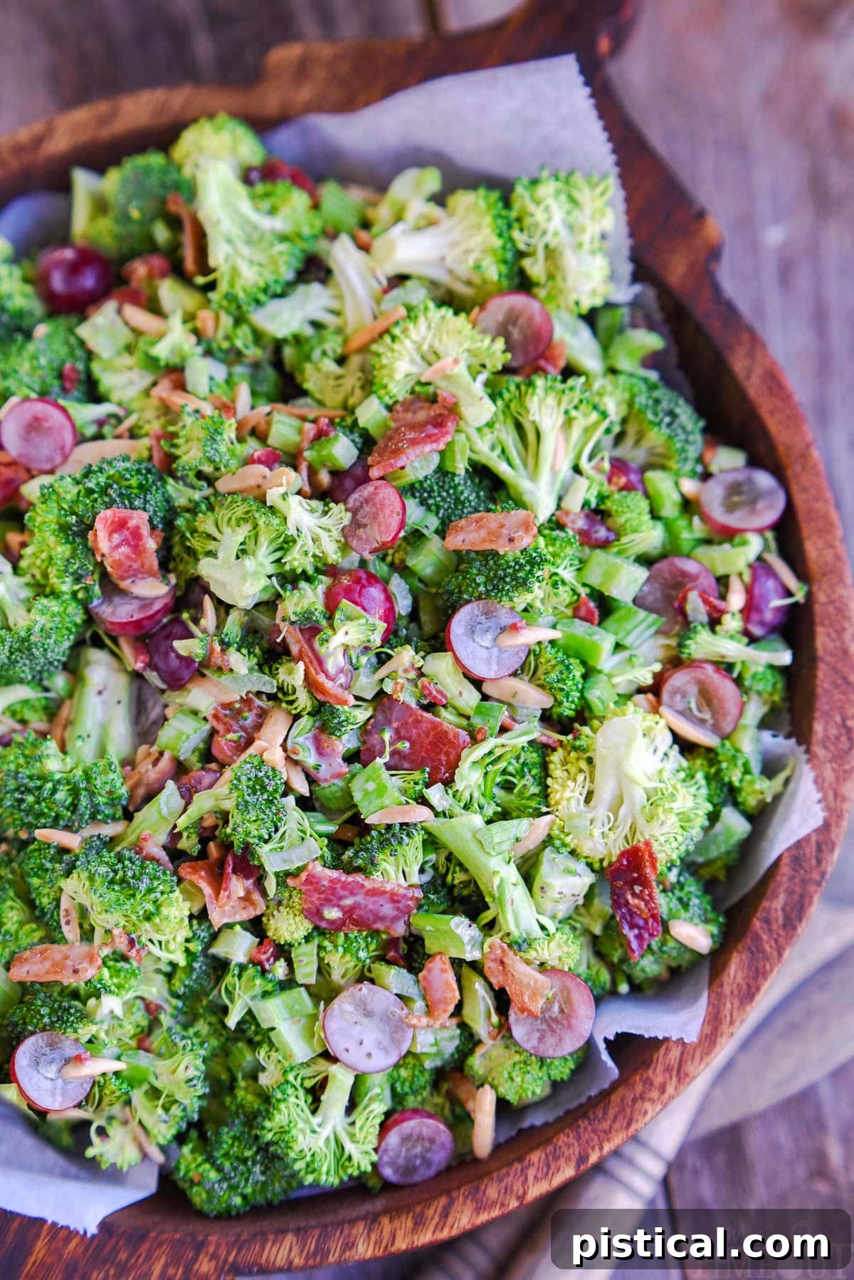 top down view of broccoli salad with bacon in a large wood bowl. Red grapes and toasted almonds can be seen tossed in the salad.