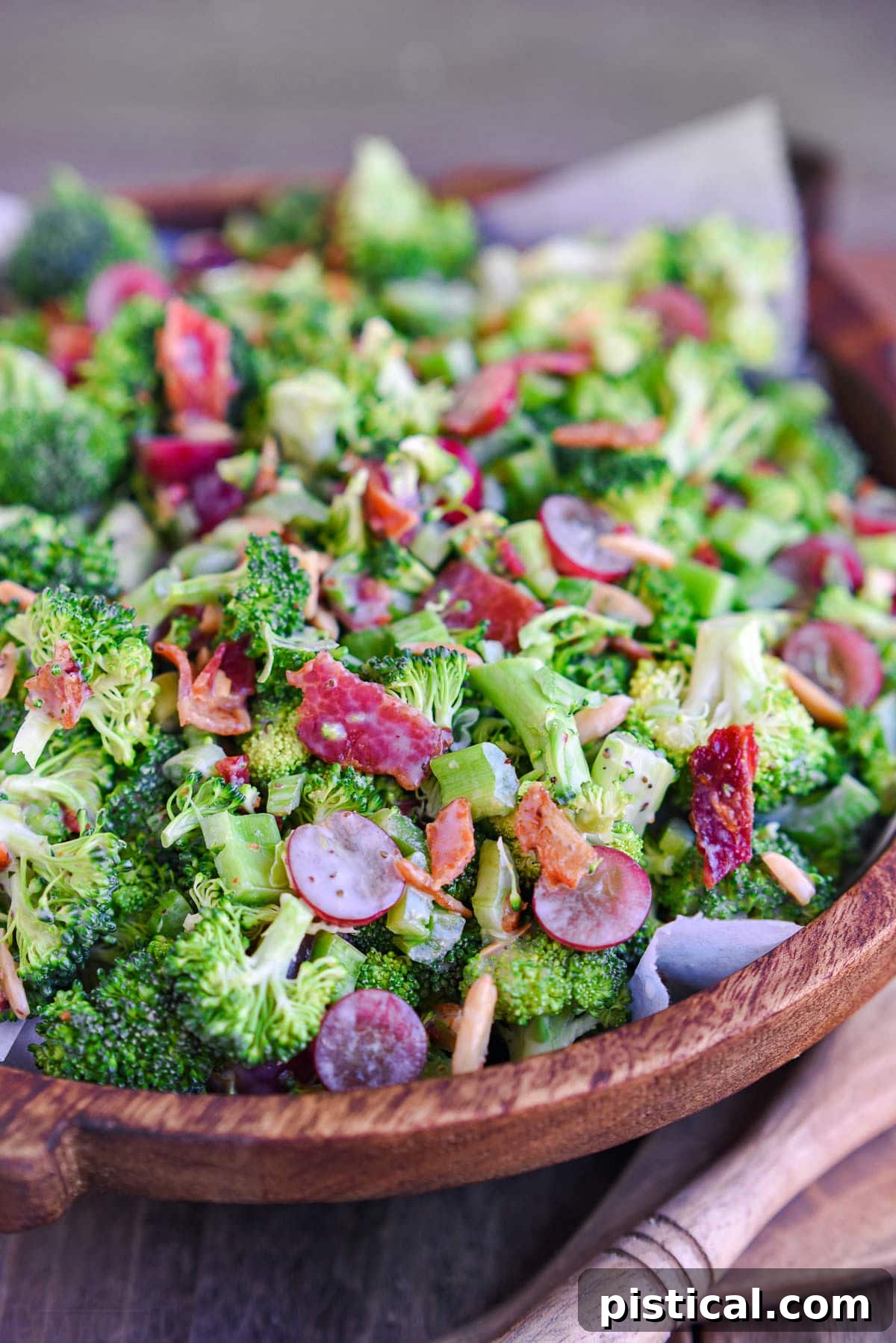 dark brown wood bowl filled with freshly prepare broccoli salad recipe made with grapes and bacon. 