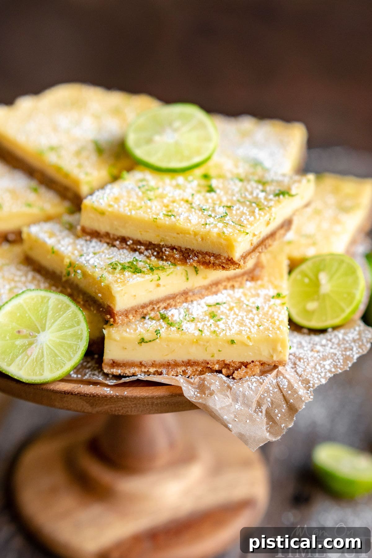 Zesty Key Lime Squares 2 A beautiful wood cake stand showcasing a stack of freshly baked Key Lime Pie Bars, garnished with vibrant key lime zest and a light sprinkle of powdered sugar. Slices of fresh lime are artfully arranged around the base, highlighting the dessert's zesty essence.