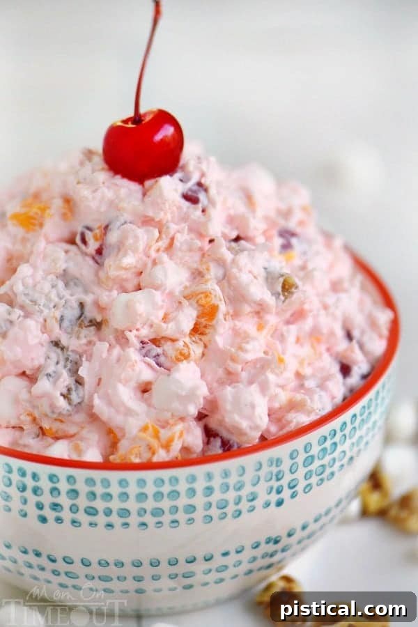 A vibrant bowl of classic Ambrosia Salad, overflowing with mandarin oranges, crushed pineapple, maraschino cherries, coconut, and fluffy marshmallows, ready to be served at a party or potluck.