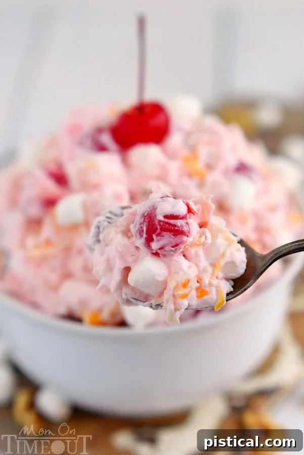 Close-up of Ambrosia Salad showing the rich texture of the creamy base, sweet mandarin oranges, red maraschino cherries, and fluffy marshmallows, emphasizing its delicious appeal.