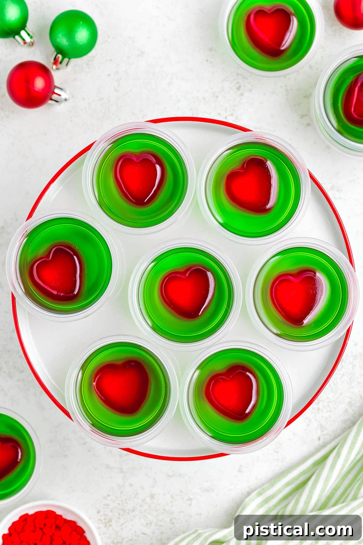 A top down view of grinch jello shots on a white plate with a red rim.