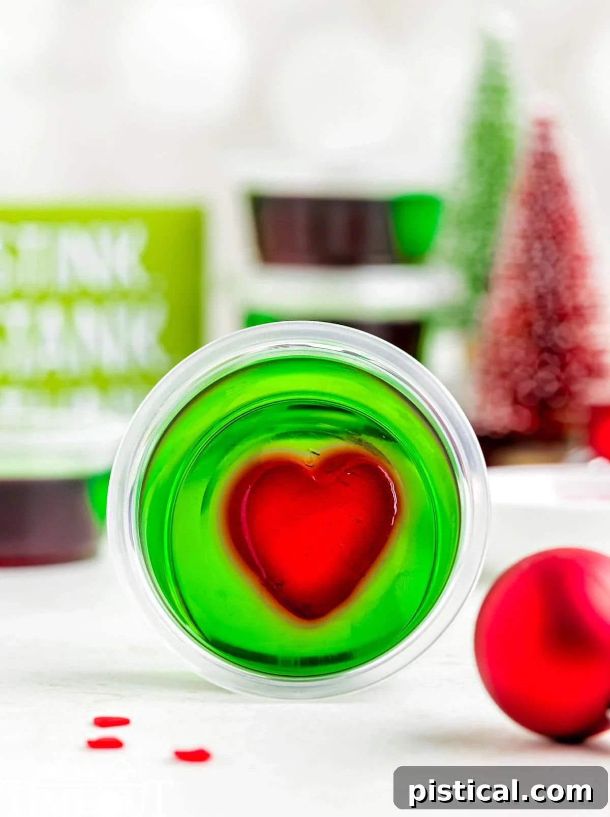 A green and red grinch jello shot in a shot glass laying on its side. Christmas decorations are in the background.