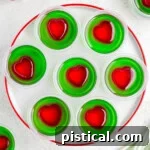 A top down view of grinch jello shots on a white plate with a red rim.