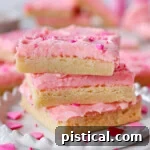 Three sugar cookie bars decorated for valentine's day stacked on white plate.