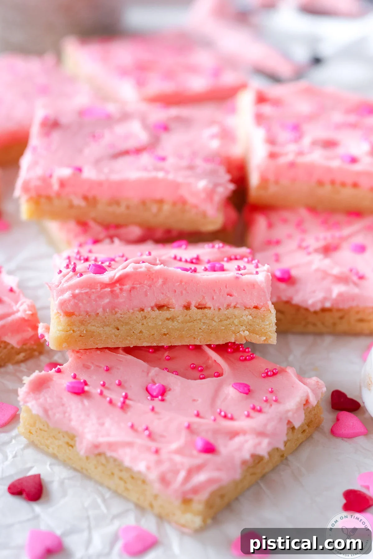 Sugar cookie bars laid out on white parchment. Bars have pink frosting and sprinkles.