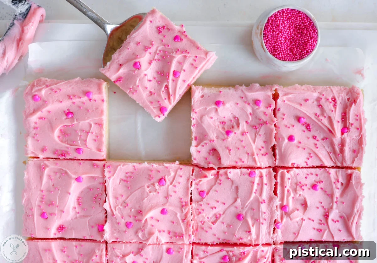 Valentine's Day Sugar Cookie Bars cut into squares on white parchment paper. One bar is being lifted away.