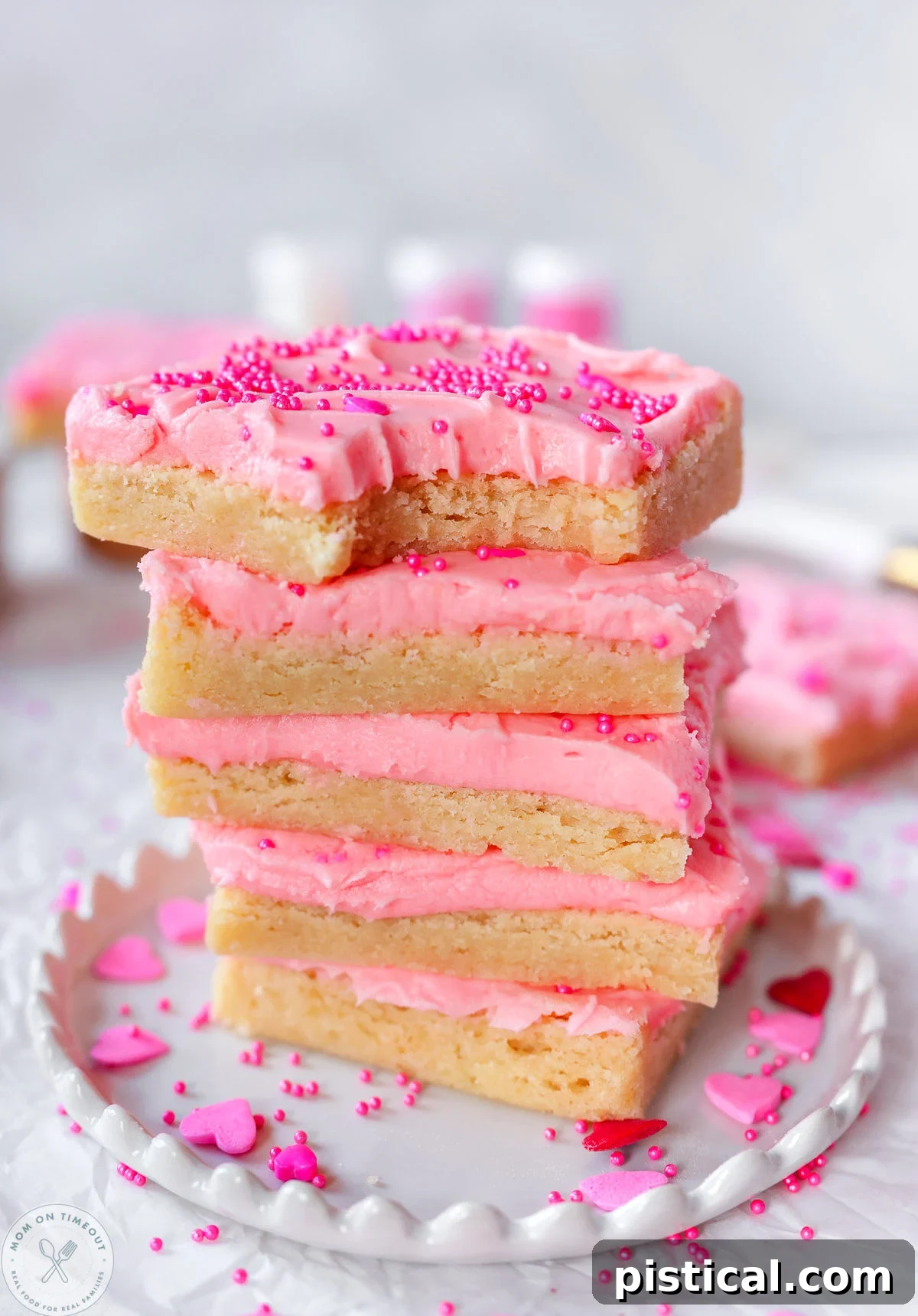 Stack of four sugar cookie bars frosted with cherry frosting and topped with sprinkles. 