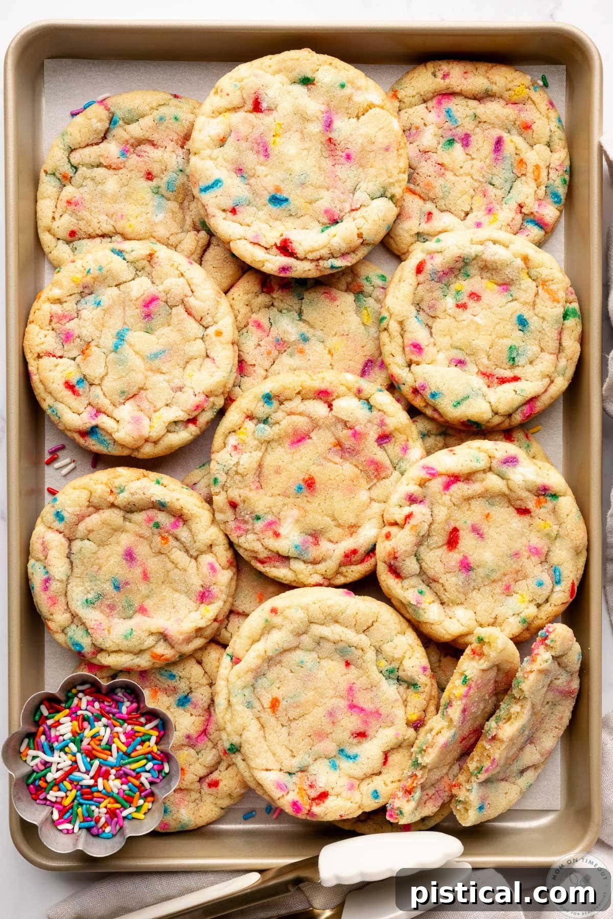 Sprinkle cookies on gold baking sheet with small bowl of jimmies sitting next to the cookies.