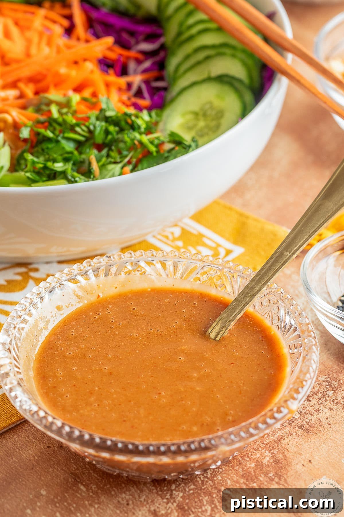 Thai peanut dressing in a small glass bowl in front of a bowl of salad.