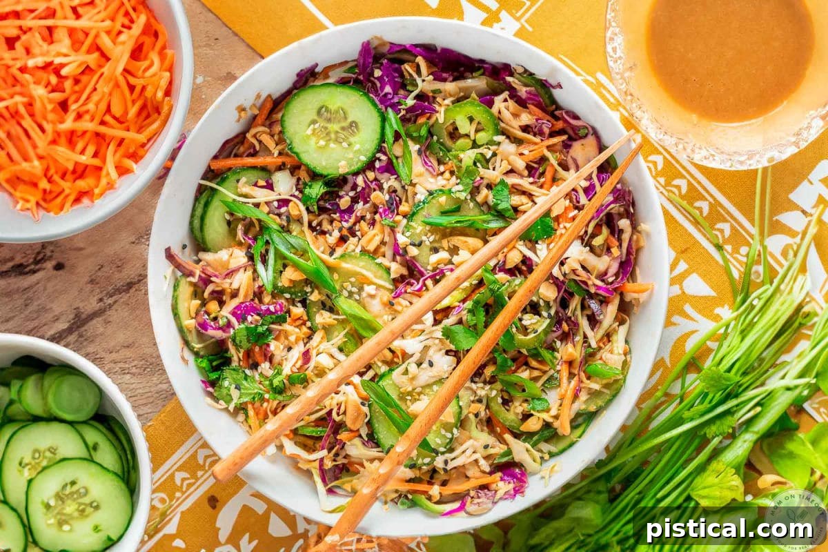 Overhead shot of large white bowl with summer thai salad that has been tossed with peanut dressing. Two chopsticks are laid on top of the bowl.