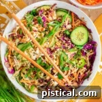 Overhead shot of large white bowl with summer thai salad that has been tossed with peanut dressing. Two chopsticks are laid on top of the bowl.