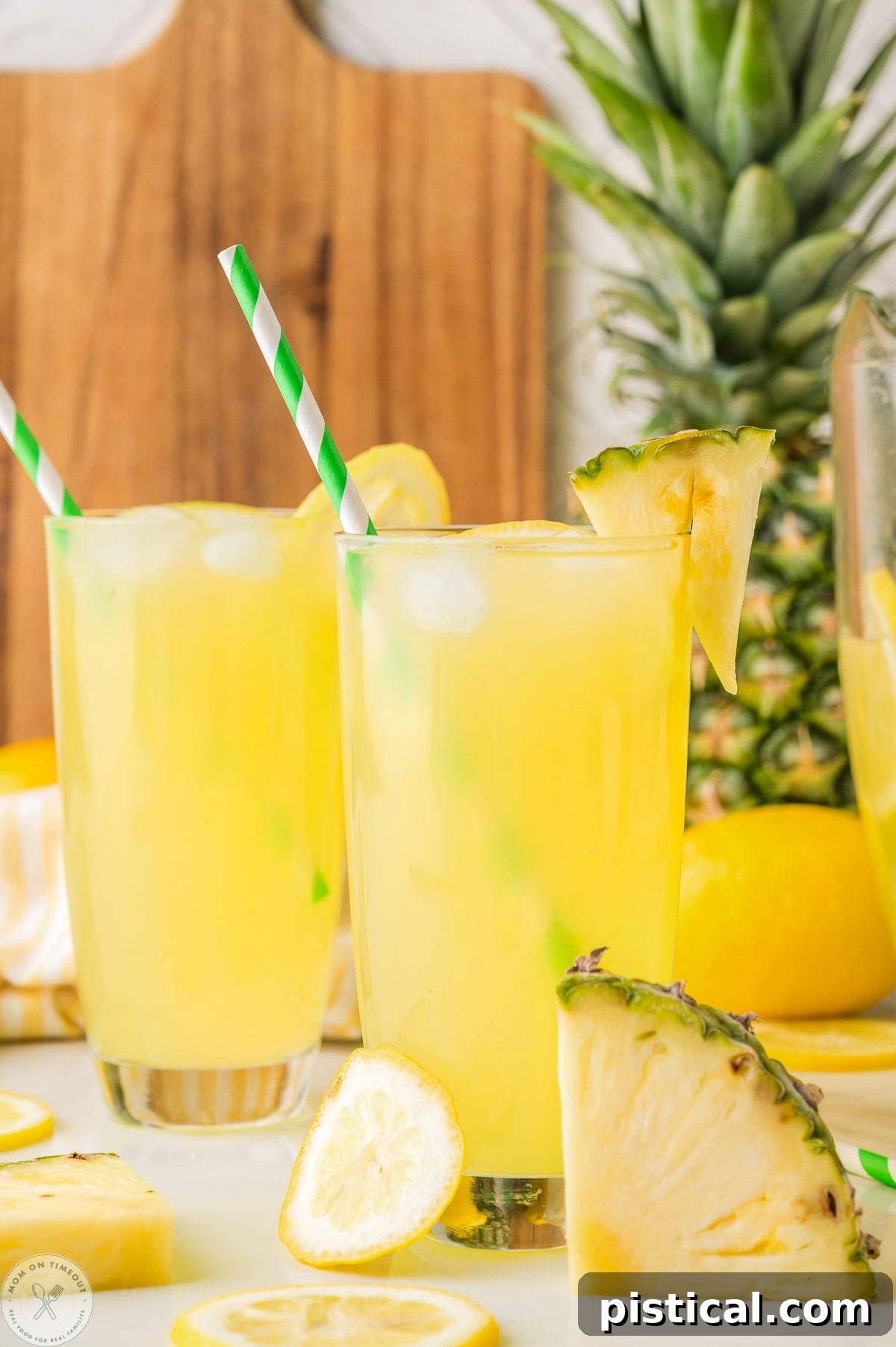 Two glasses filled with pineapple lemonade. Straws in glasses with fresh pineapple in the background.