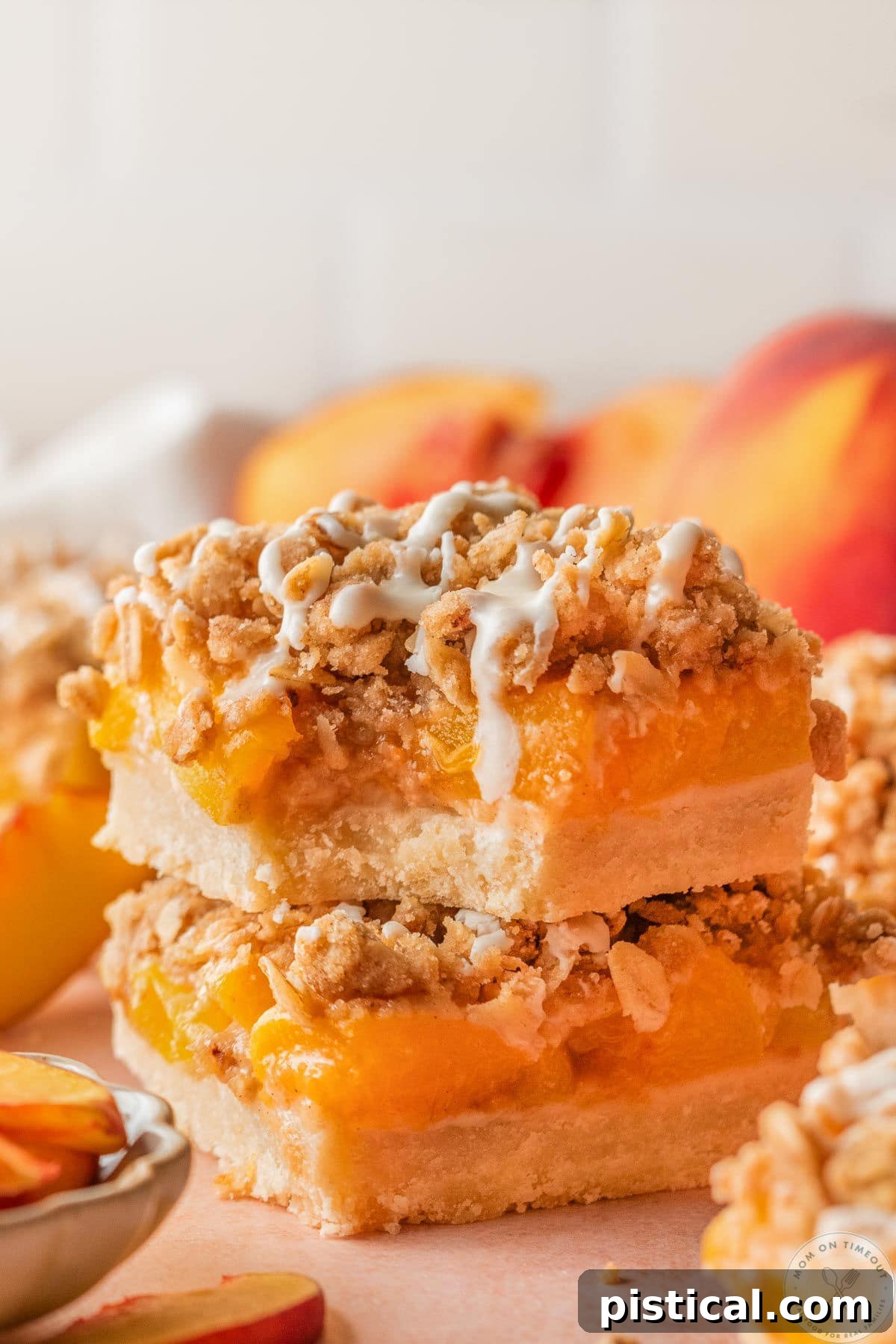 Peach Crumble Bars with Buttery Streusel Topping 2 Close up of two peach pie bars stacked on scalloped dessert plate. Topped with a drizzle and top bar has a bite taken.