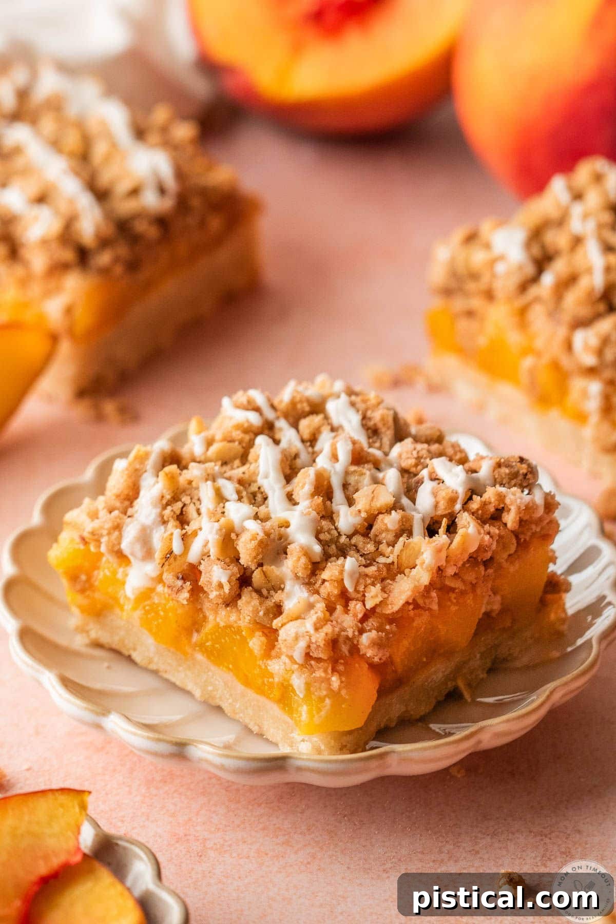 Peach Crumble Bars with Buttery Streusel Topping 3 Single peach crumb bar with a vanilla glaze cut into a square sitting on round dessert plate with more bars in the background.