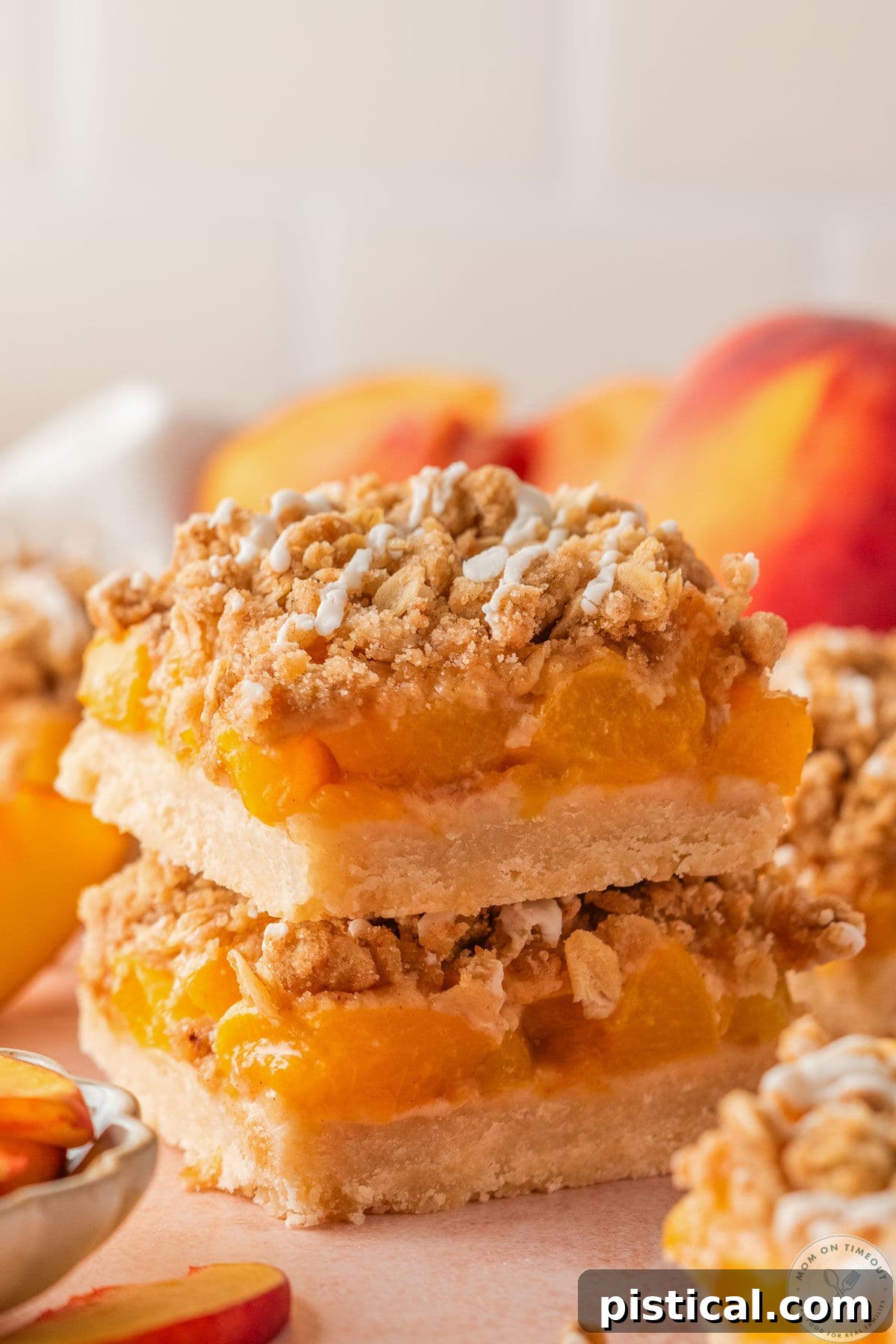 Peach Crumble Bars with Buttery Streusel Topping 4 Two whole peach pie crumb bars stacked on each with peaches in the background.