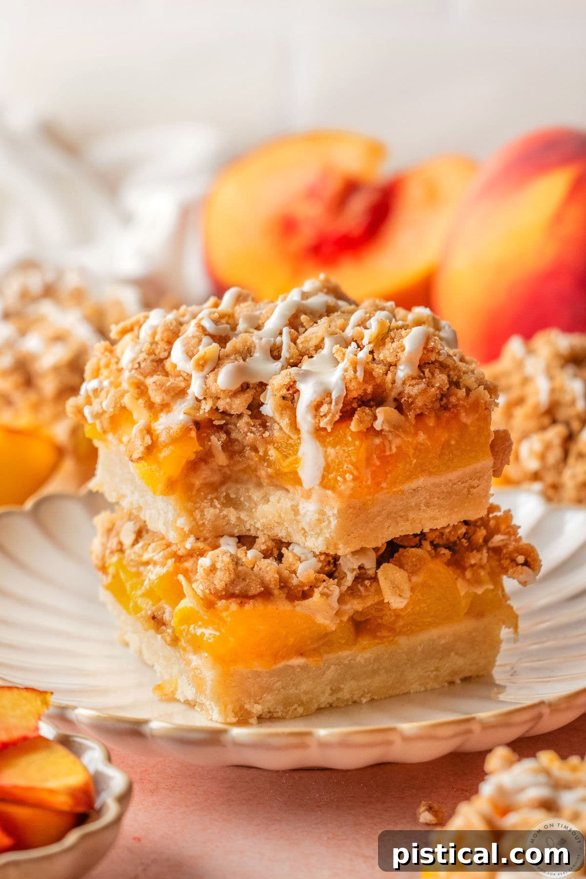 Peach Crumble Bars with Buttery Streusel Topping 6 Two peach pie bars stacked on scalloped dessert plate. Topped with a drizzle and top bar has a bite taken.