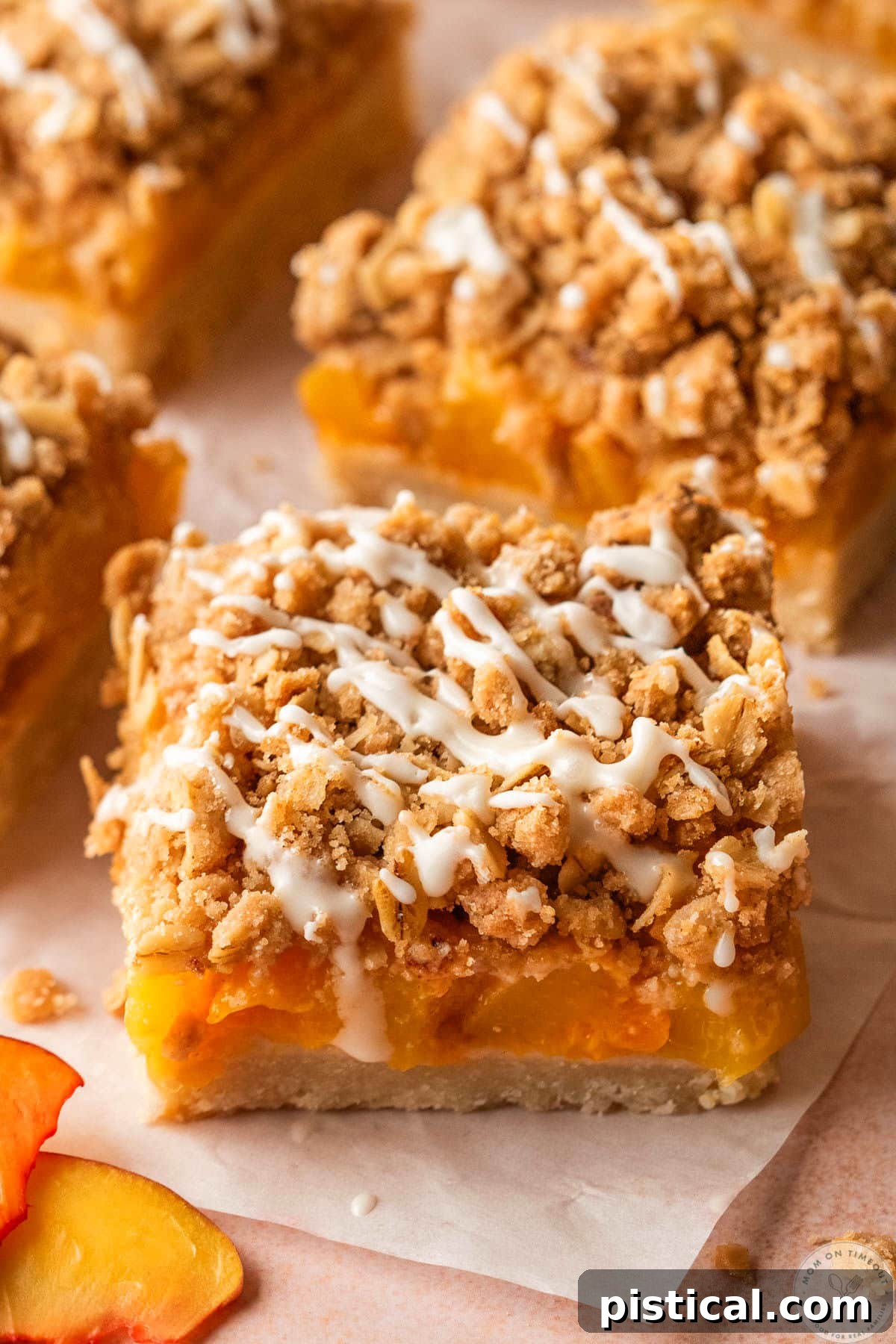 Peach Crumble Bars with Buttery Streusel Topping 7 Peach Crumb Bars cut into square and sitting on parchment squares. The bars are drizzled with a glaze.