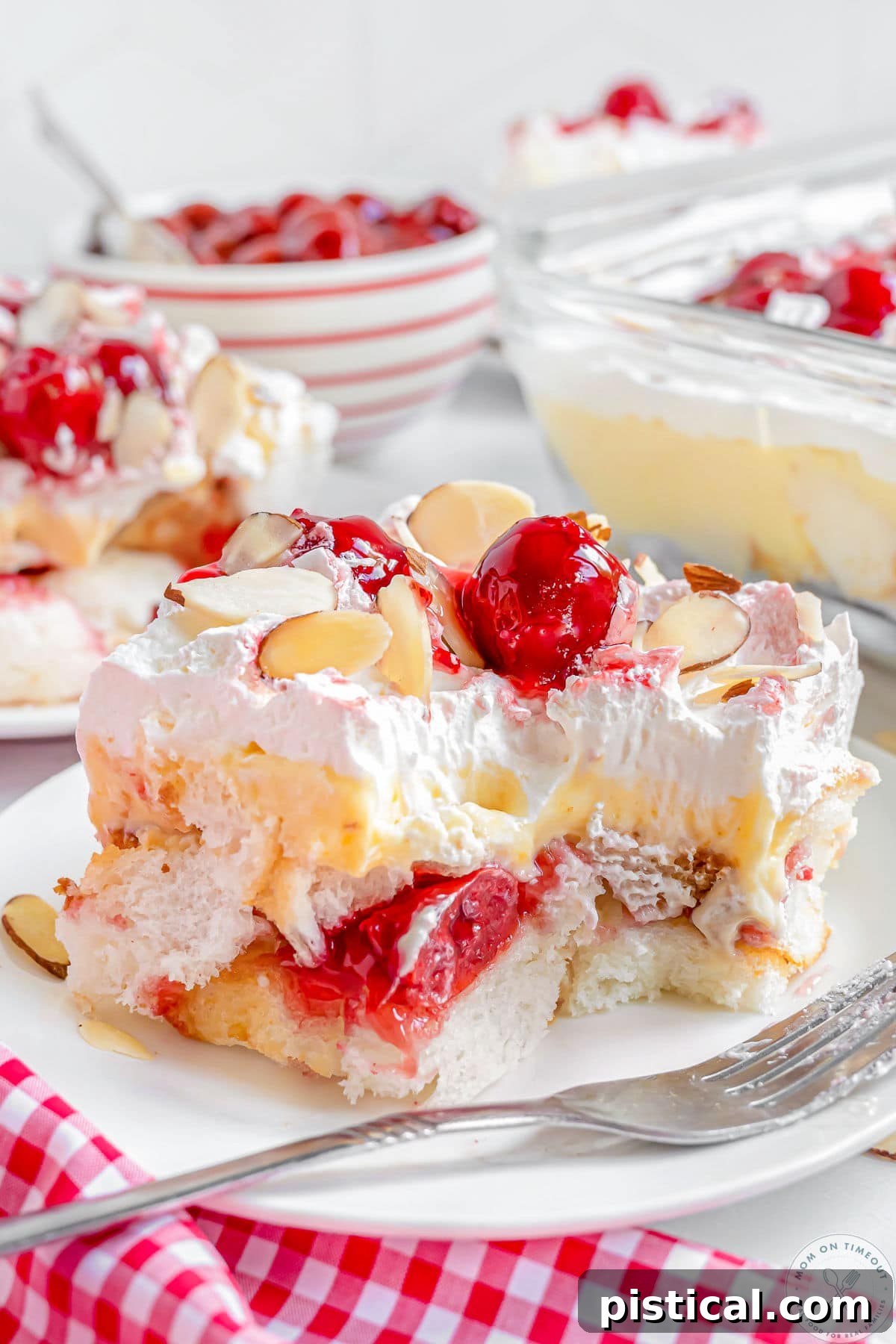 Layered Heaven On Earth Cake on a white plate with fork. Bright red cherries and almonds on top.