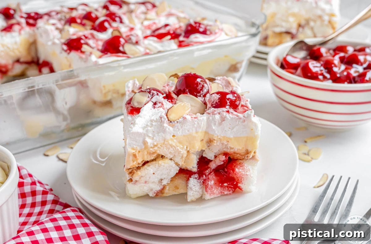 Angel food cake slice topped with cherry pie filling and almonds on a white plate.