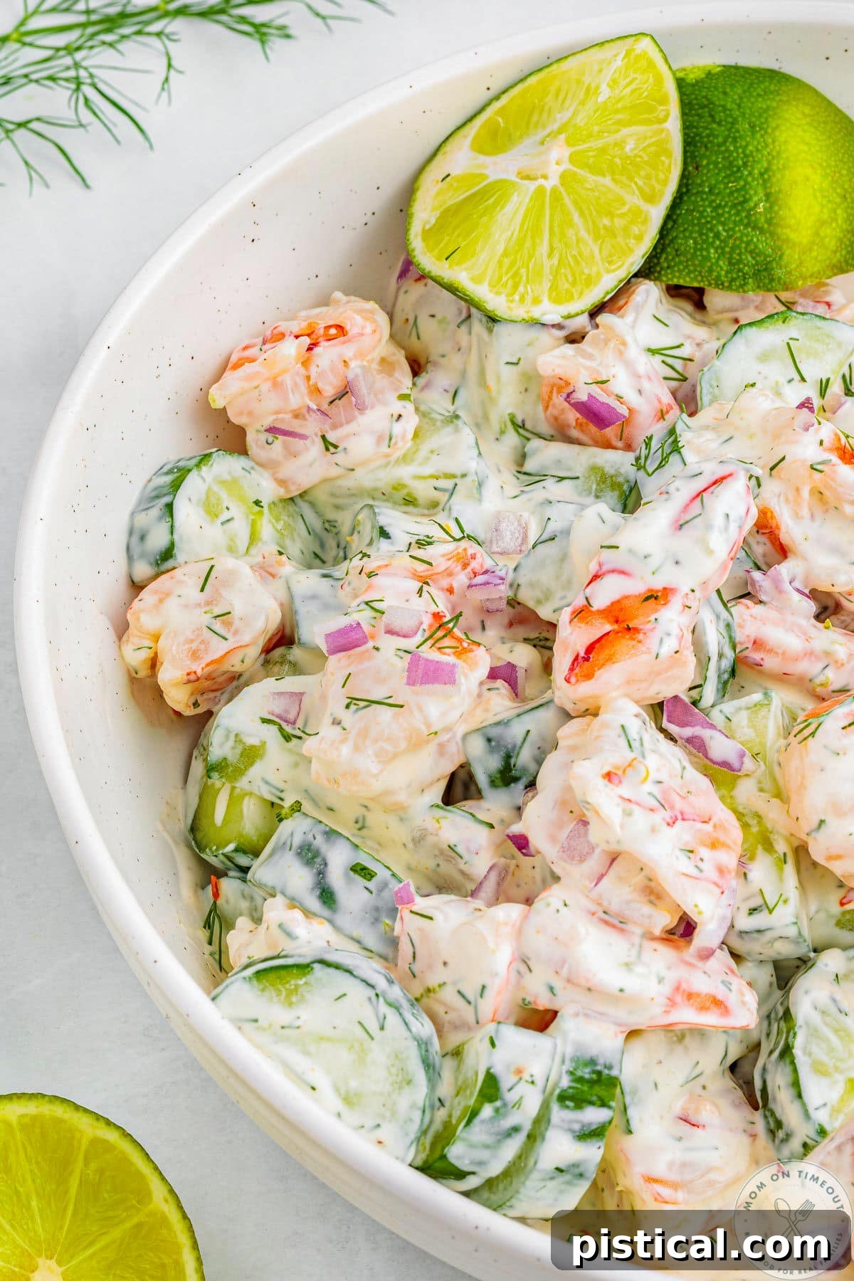 Overhead shot of half of white bowl filled with shrimp and cucumber salad. Two lime wedges are tucked into the salad.
