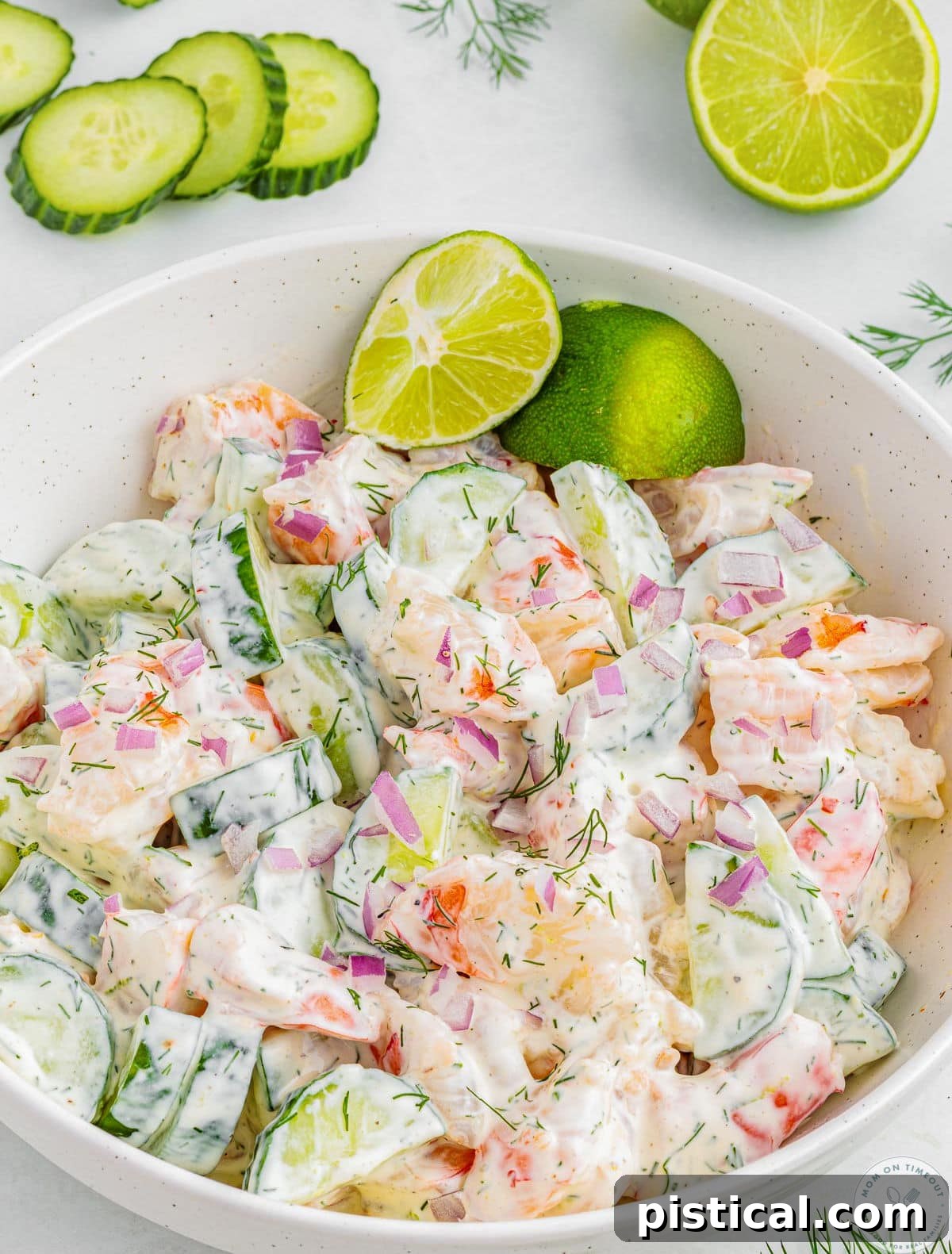 Shrimp cucumber salad in shallow white bowl garnished with lime wedges. Serving spoon sat off to the side.