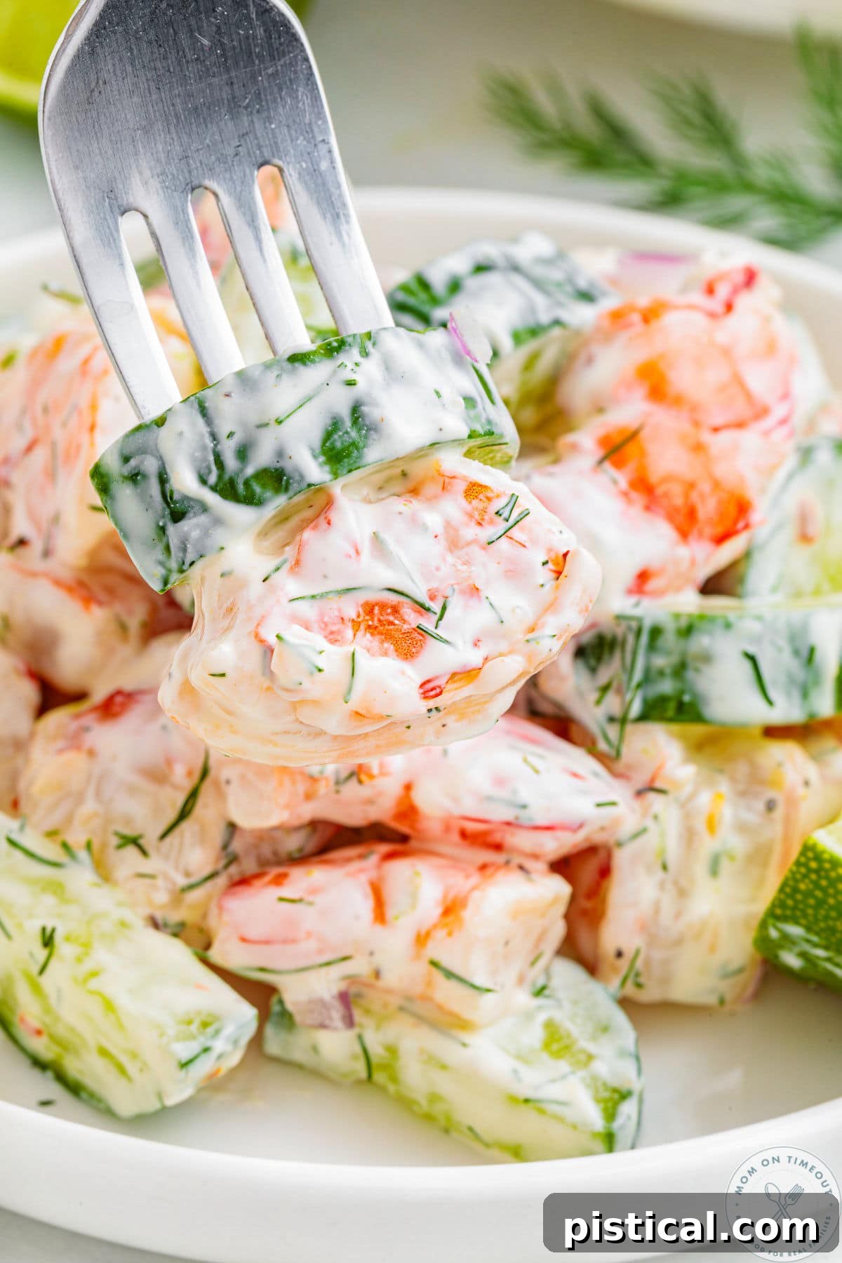 Creamy cucumber shrimp salad in bowl with fork piercing one piece of cucumber and shrimp.